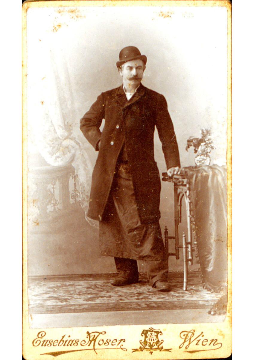 Eusebius Moser, Herr mit Hut, Mantel und Schürze am Tisch lehnend, Inv. Nr.: Foto2013/171/180